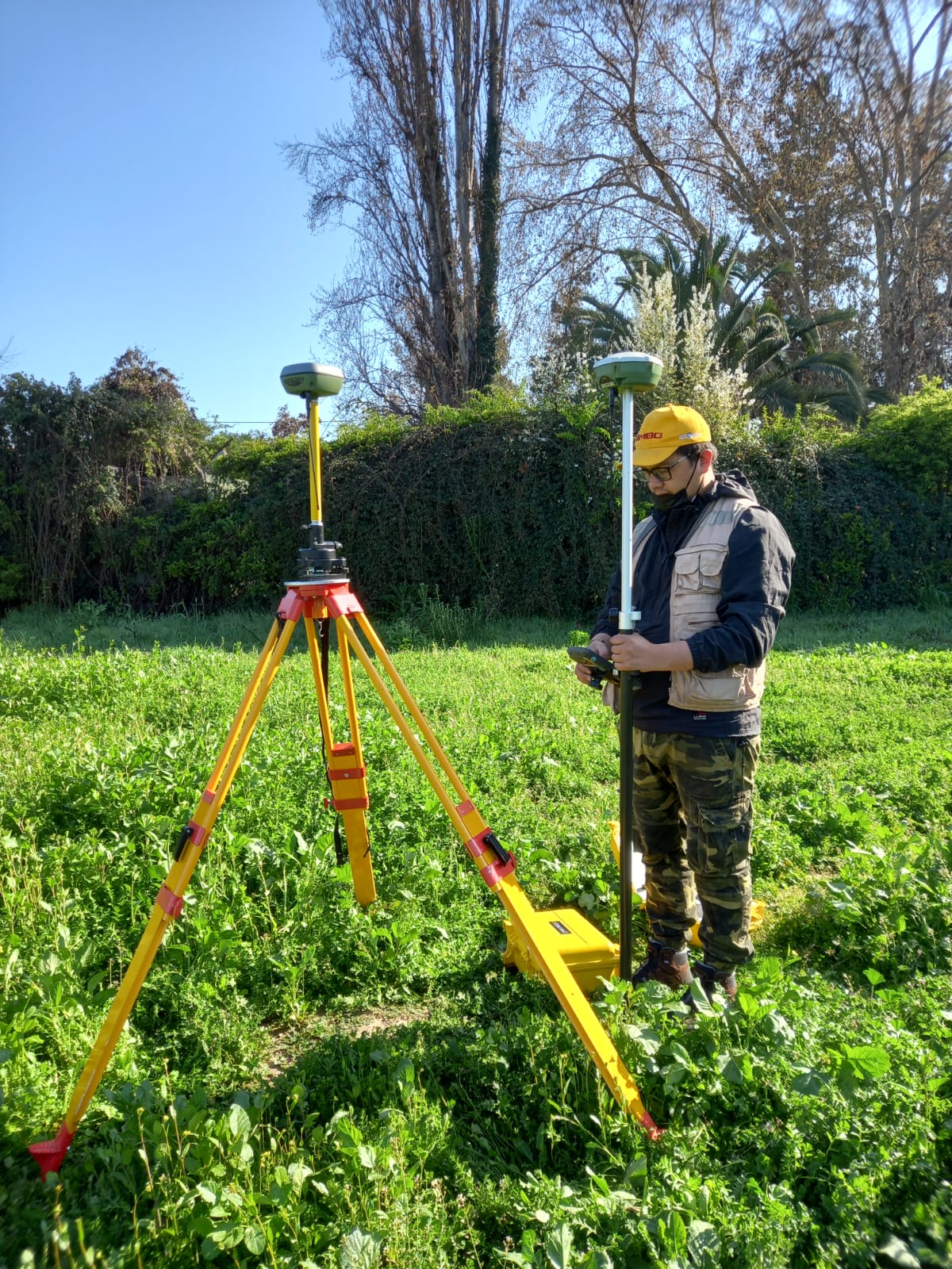 Topógrafo de topografiachile.cl con casco amarillo, chaleco de campo y receptor GPS RTK junto a la estación base en terreno